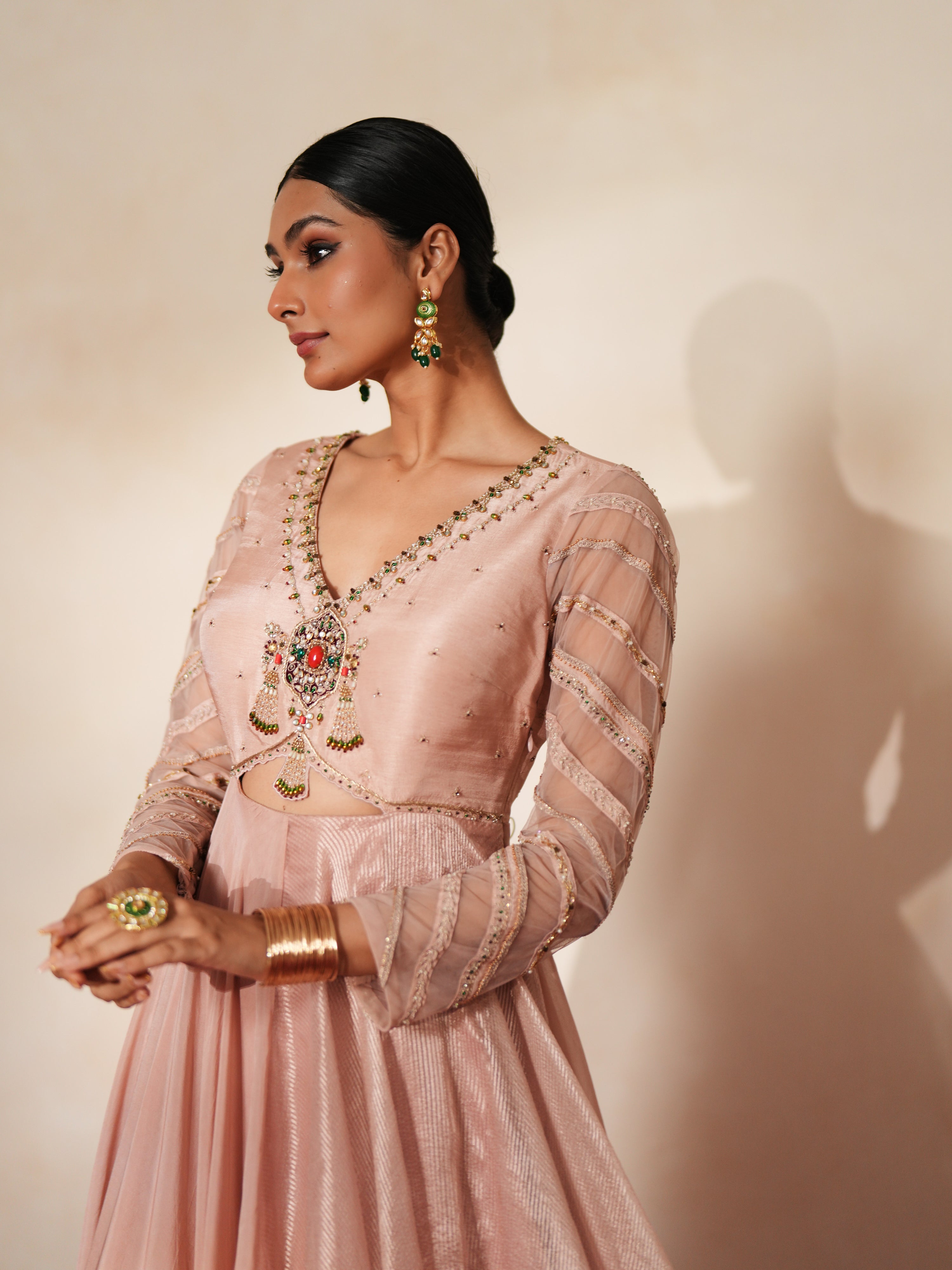 Woman in a soft pink traditional outfit standing againsta beige wall on a red carpet.