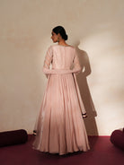 Woman in a soft pink traditional outfit standing againsta beige wall on a red carpet.