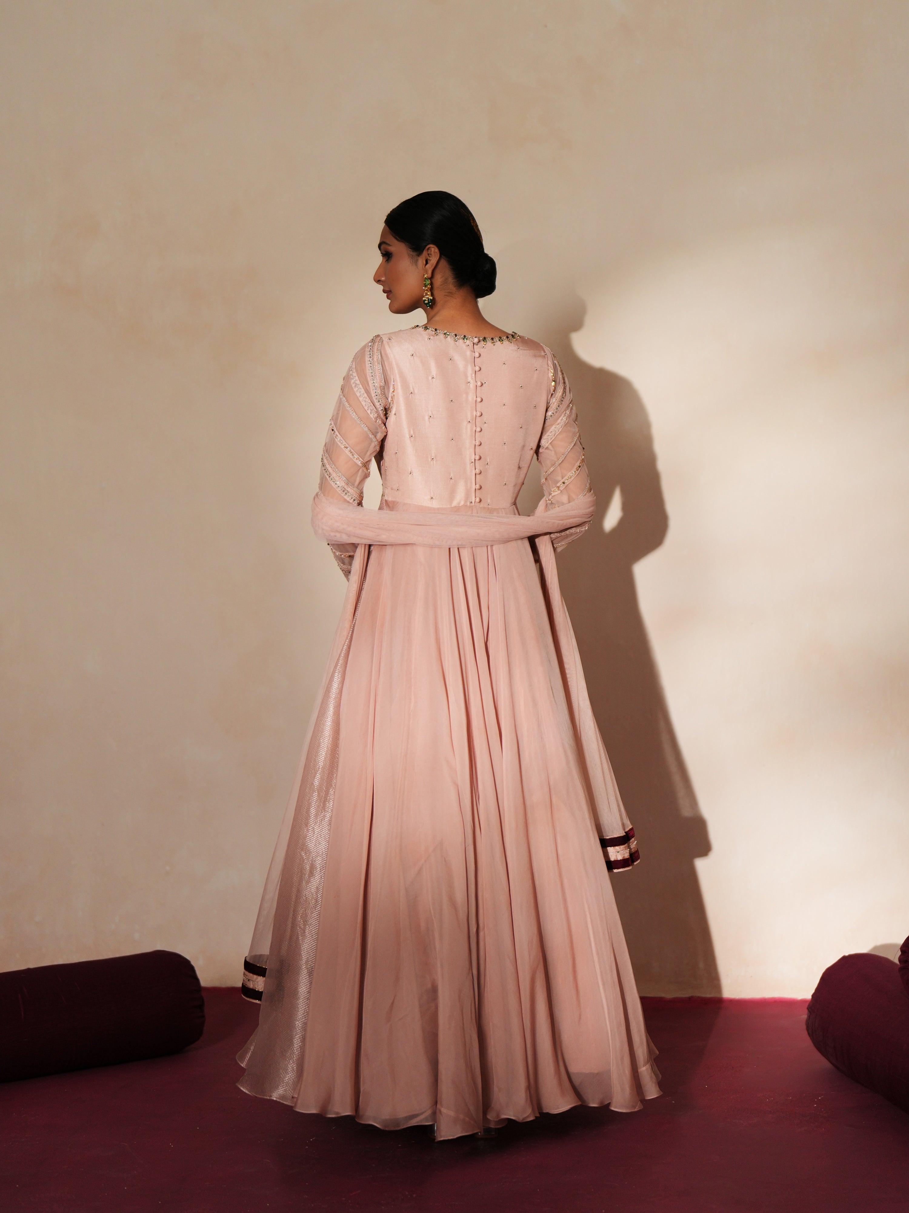 Woman in a soft pink traditional outfit standing againsta beige wall on a red carpet.