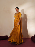 Woman in a golden yellow traditional outfit standing againsta beige wall on a red carpet.