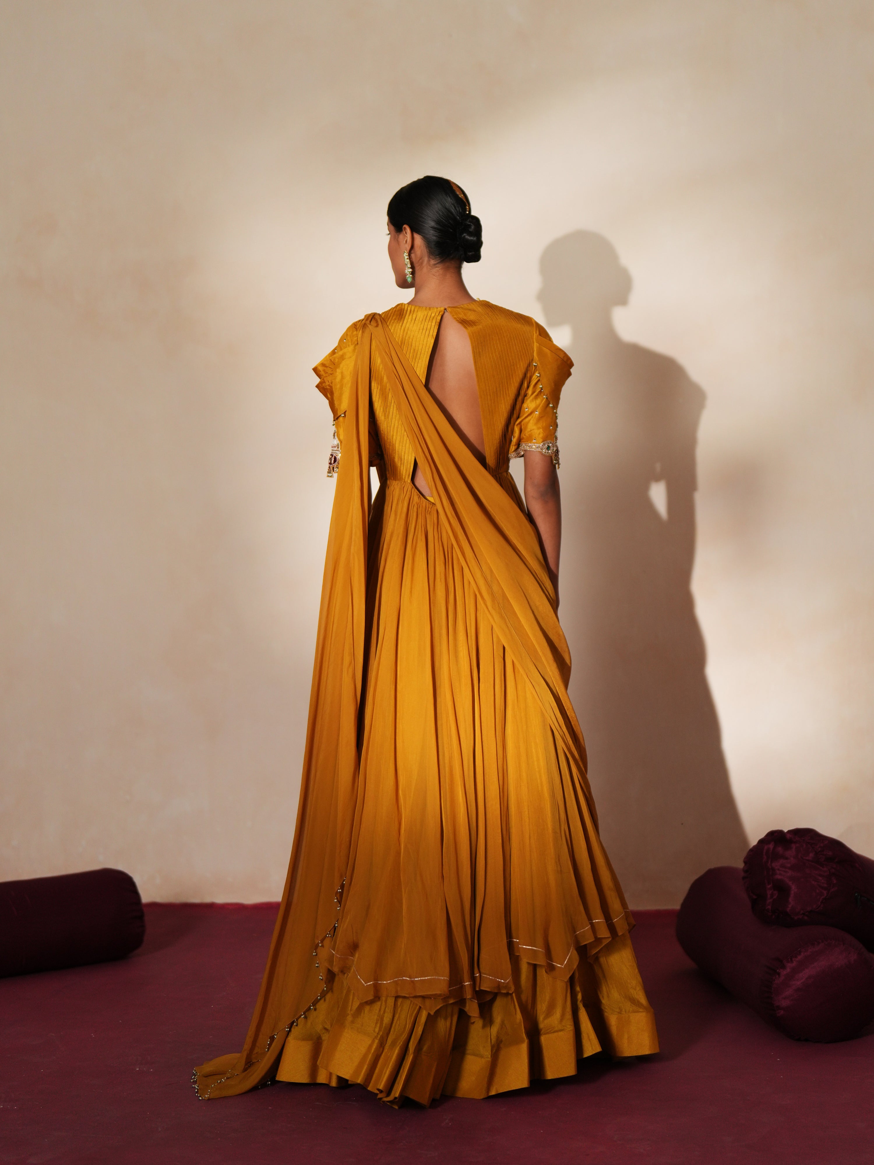 Woman in a golden yellow traditional outfit standing againsta beige wall on a red carpet.
