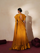 Woman in a golden yellow traditional outfit standing againsta beige wall on a red carpet.