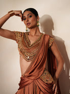 Woman in a metallic mocha  traditional outfit standing againsta beige wall on a red carpet.