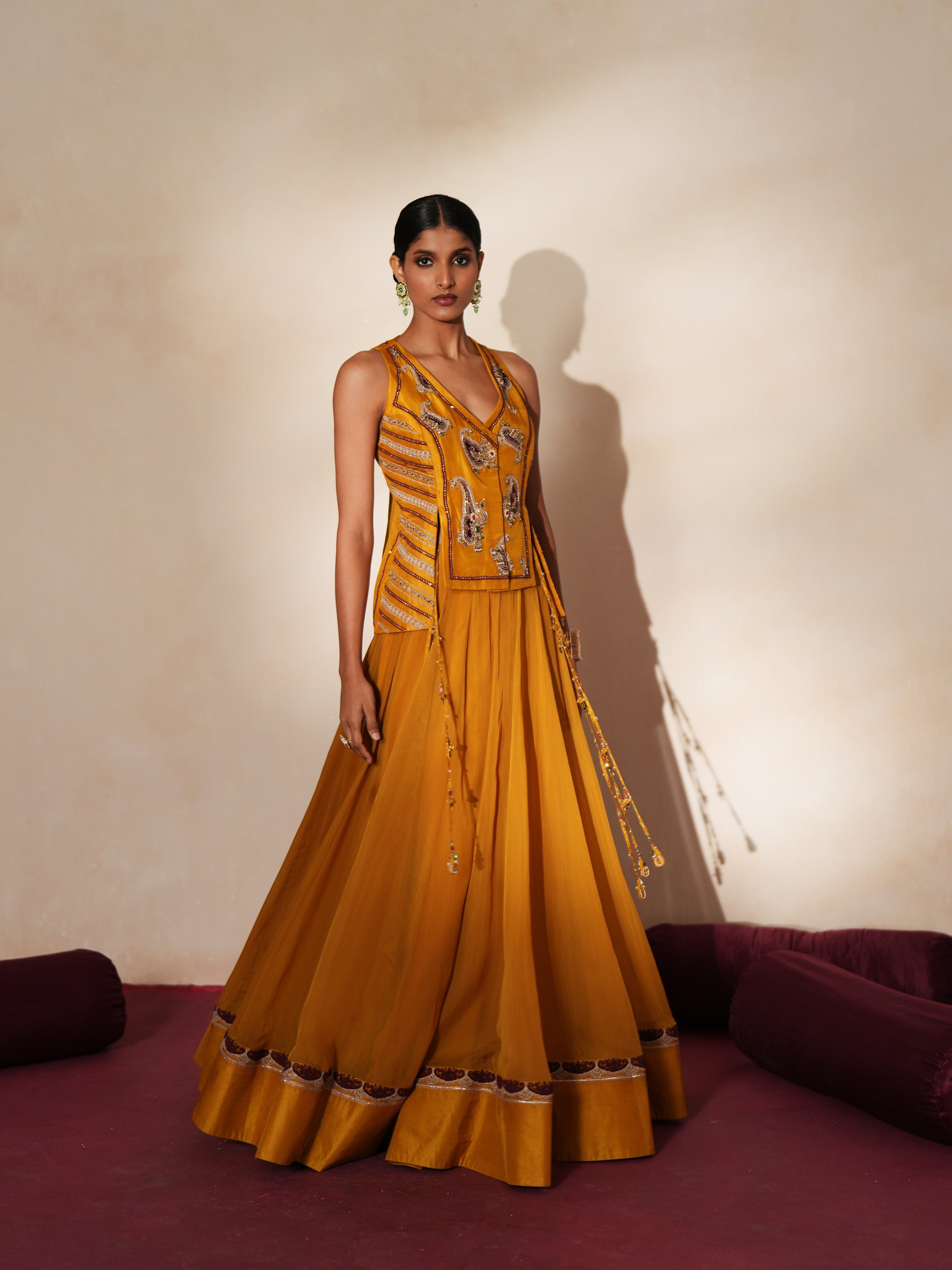 Woman in a golden yellow traditional outfit standing againsta beige wall on a red carpet.