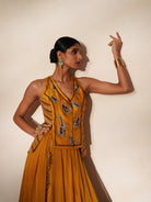 Woman in a golden yellow traditional outfit standing againsta beige wall on a red carpet.