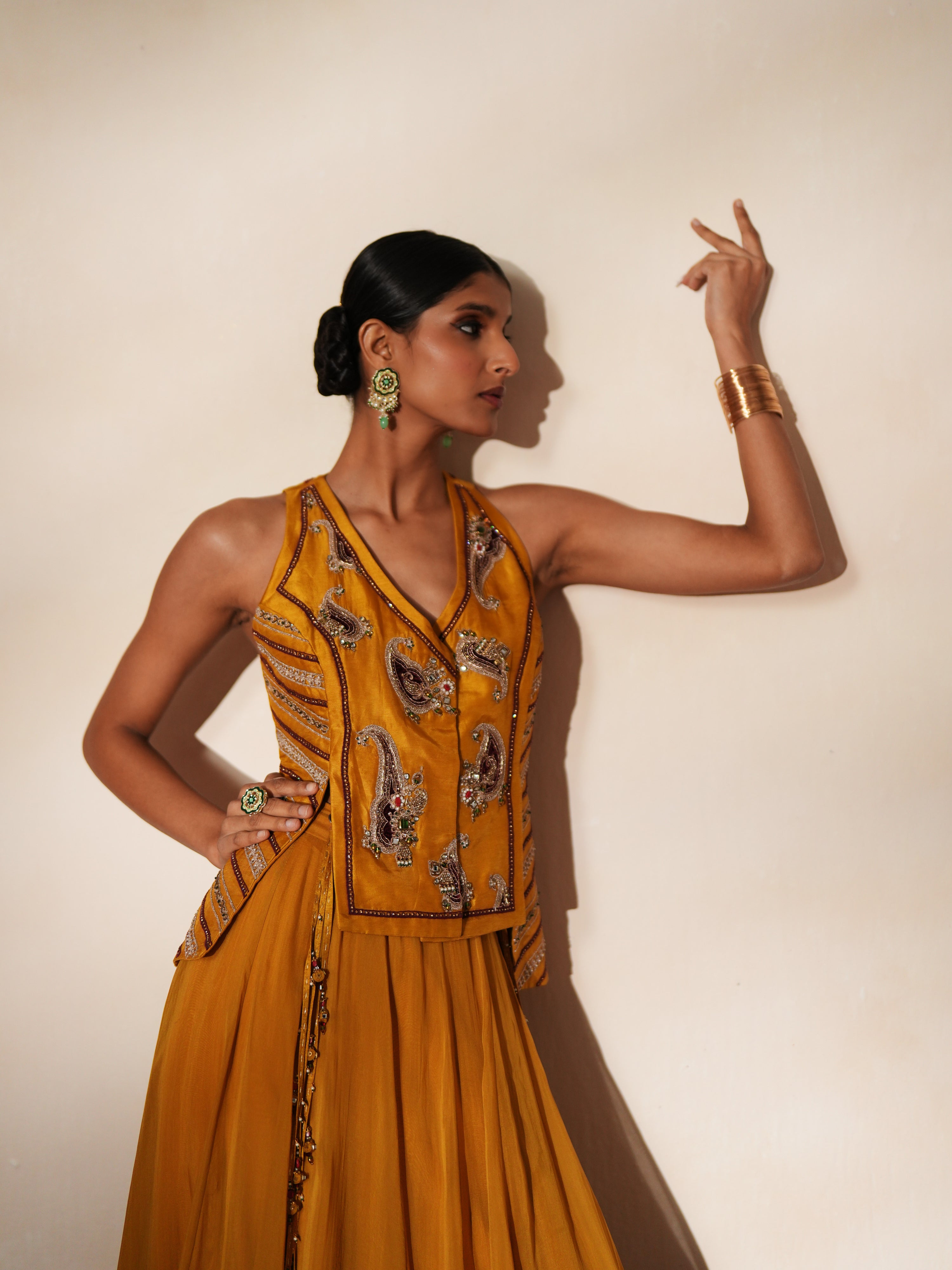 Woman in a golden yellow traditional outfit standing againsta beige wall on a red carpet.