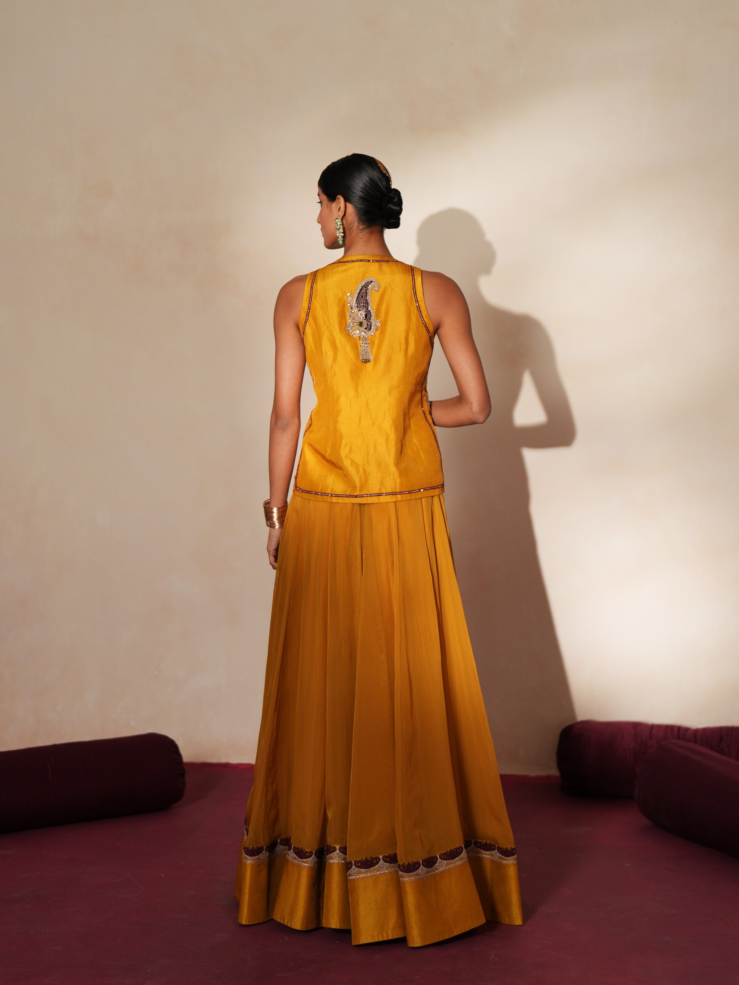 Woman in a golden yellow traditional outfit standing againsta beige wall on a red carpet.