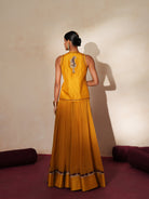 Woman in a golden yellow traditional outfit standing againsta beige wall on a red carpet.