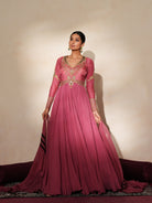 Woman in a mauve pink traditional outfit standing againsta beige wall on a red carpet.