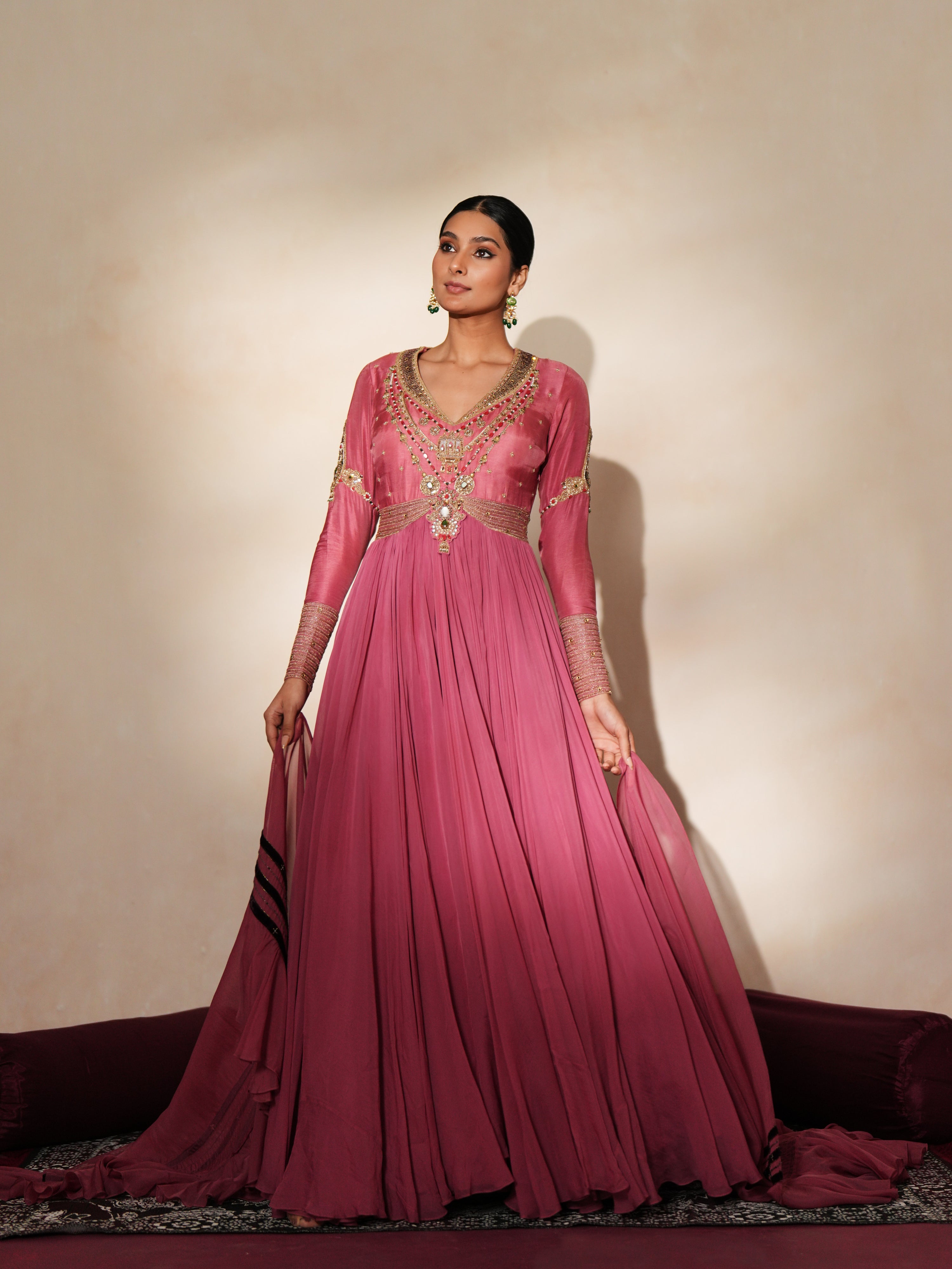 Woman in a mauve pink traditional outfit standing againsta beige wall on a red carpet.