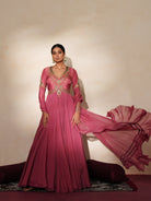 Woman in a mauve pink traditional outfit standing againsta beige wall on a red carpet.