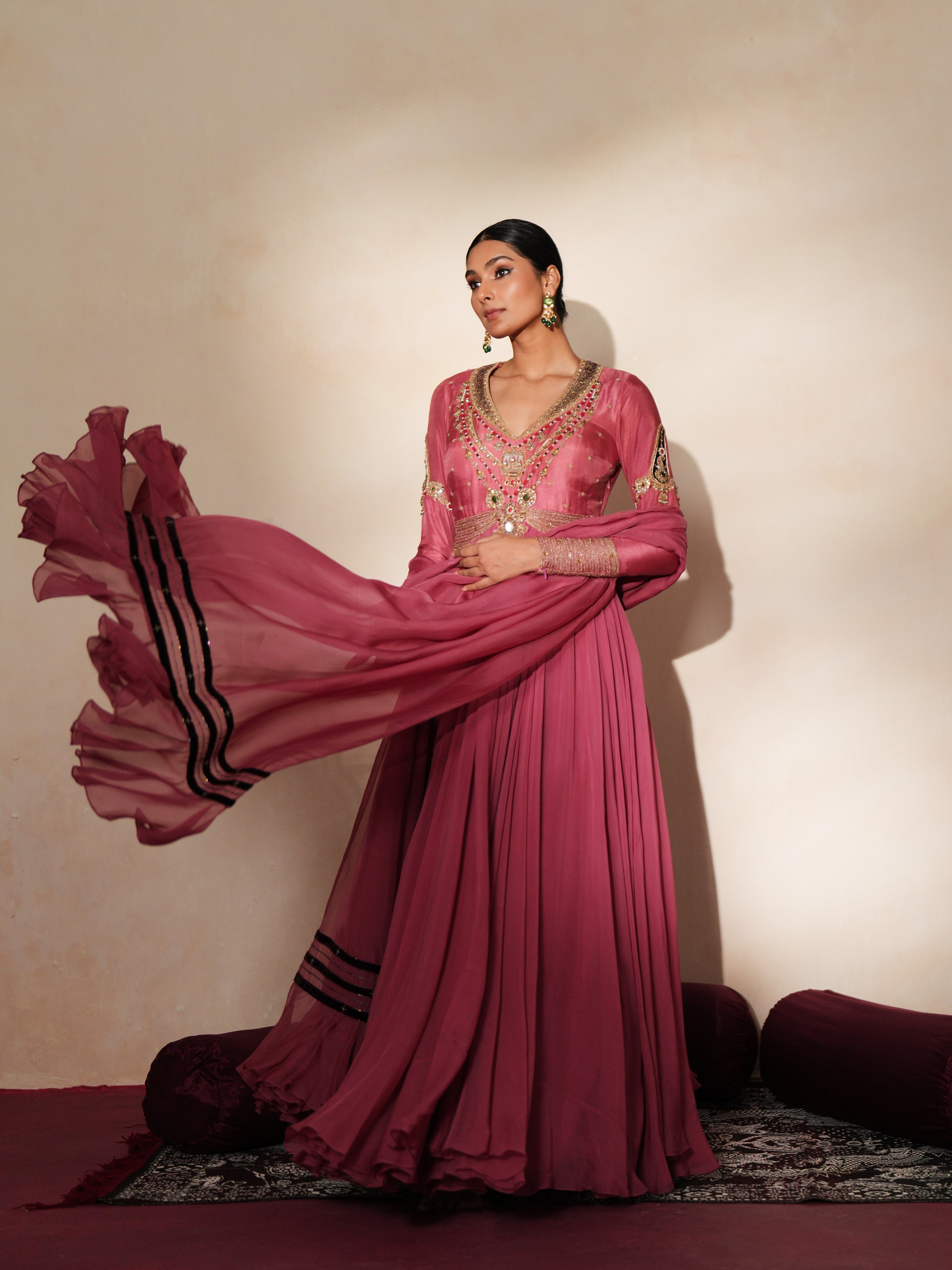 Woman in a mauve pink traditional outfit standing againsta beige wall on a red carpet.