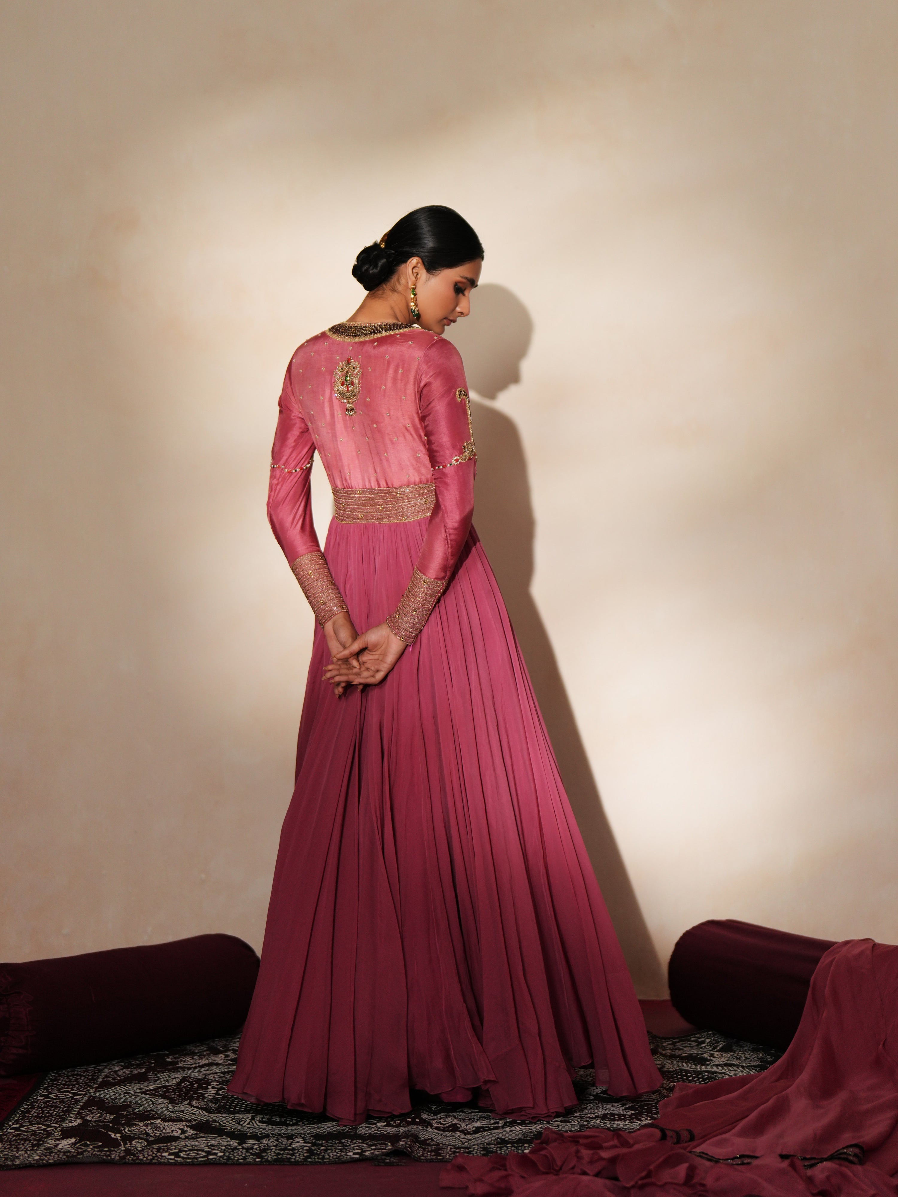 Woman in a mauve pink traditional outfit standing againsta beige wall on a red carpet.