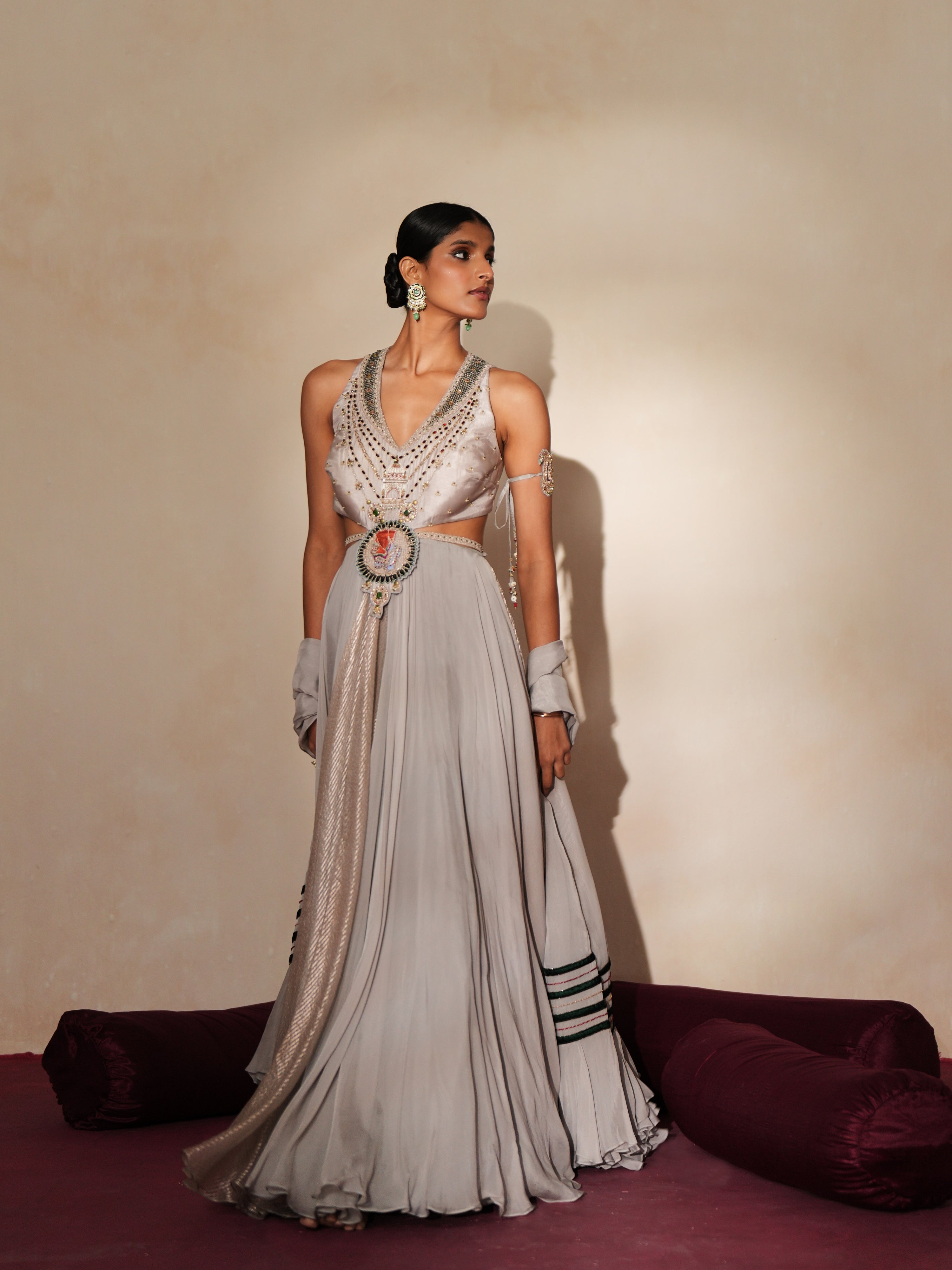 Woman in a mettalic grey traditional outfit standing againsta beige wall on a red carpet.