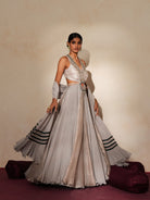 Woman in a mettalic grey traditional outfit standing againsta beige wall on a red carpet.