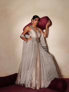Woman in a mettalic grey traditional outfit standing againsta beige wall on a red carpet.