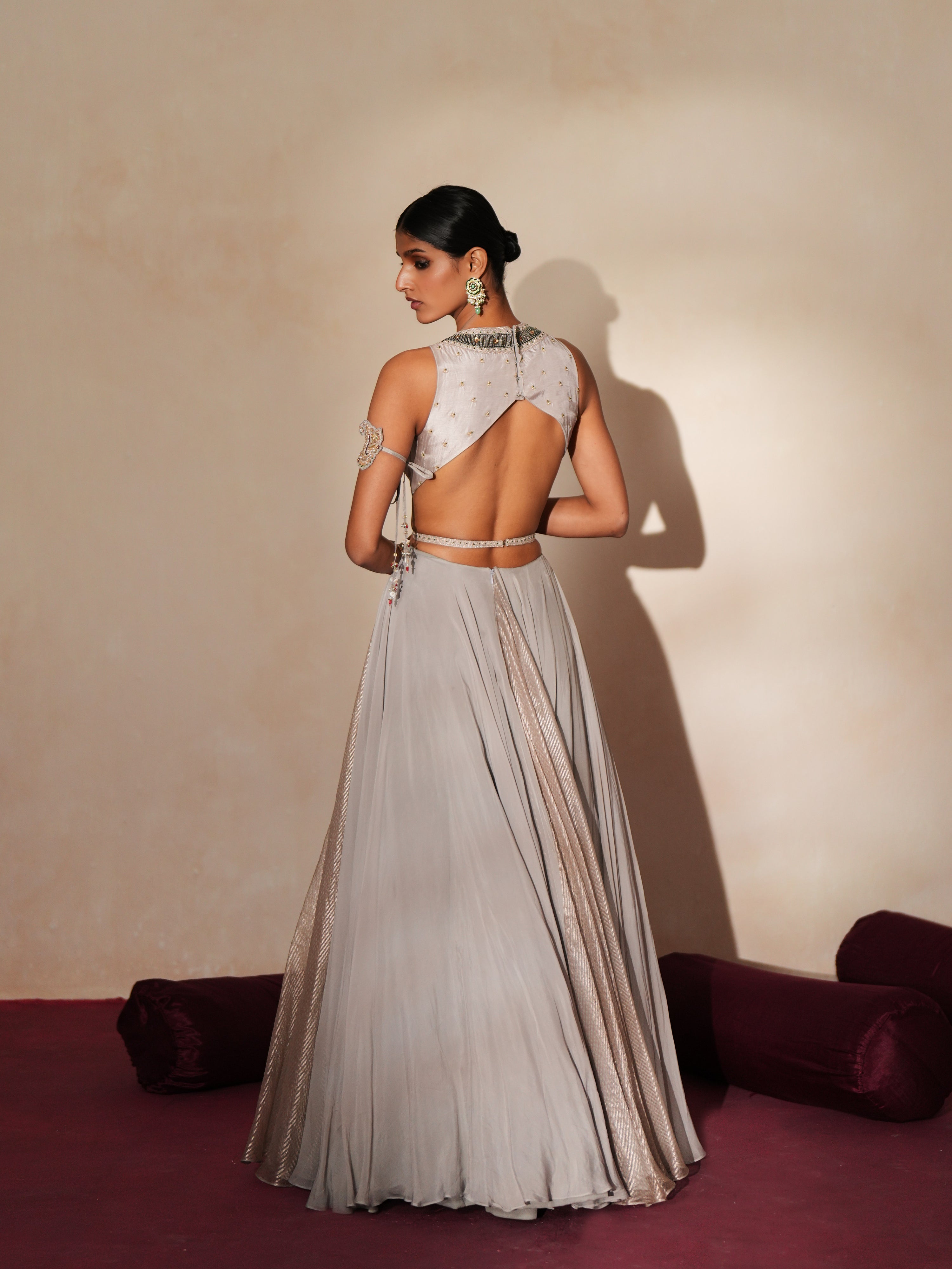 Woman in a mettalic grey traditional outfit standing againsta beige wall on a red carpet.