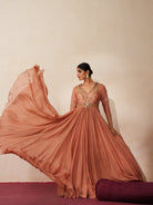 Woman in a metallic mocha  traditional outfit standing againsta beige wall on a red carpet.