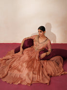 Woman in a metallic mocha  traditional outfit standing againsta beige wall on a red carpet.