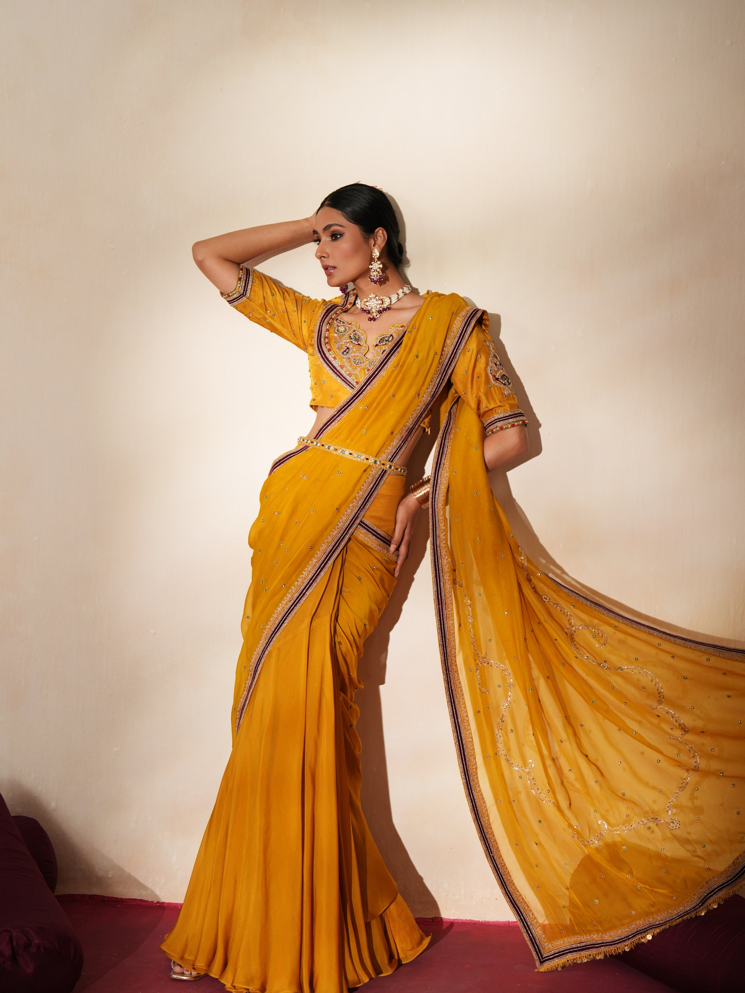 Woman in a golden yellow traditional outfit standing againsta beige wall on a red carpet.