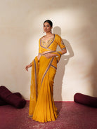 Woman in a golden yellow traditional outfit standing againsta beige wall on a red carpet.