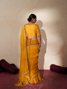 Woman in a golden yellow traditional outfit standing againsta beige wall on a red carpet.