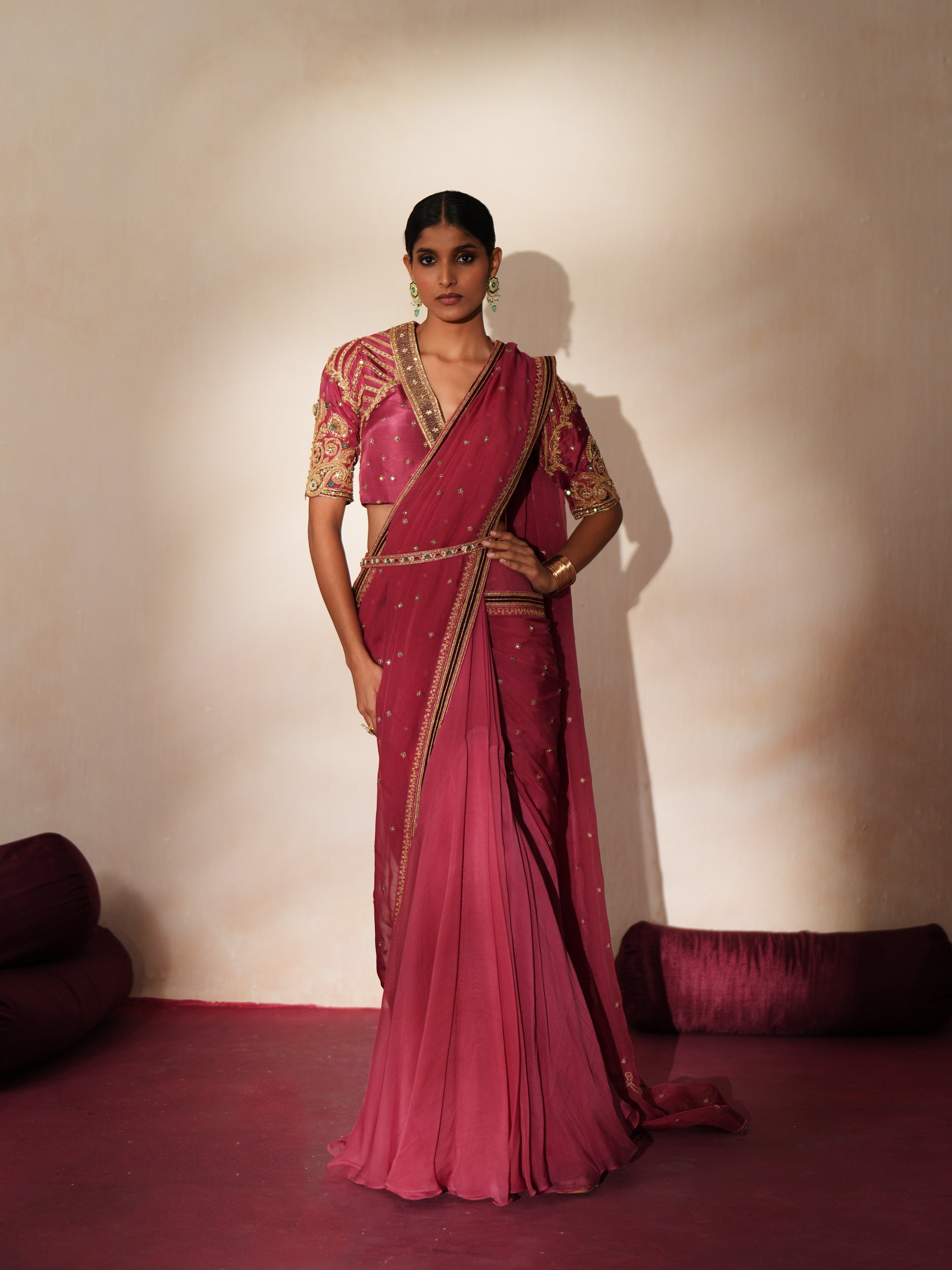 Woman in a mauve pink traditional outfit standing againsta beige wall on a red carpet.