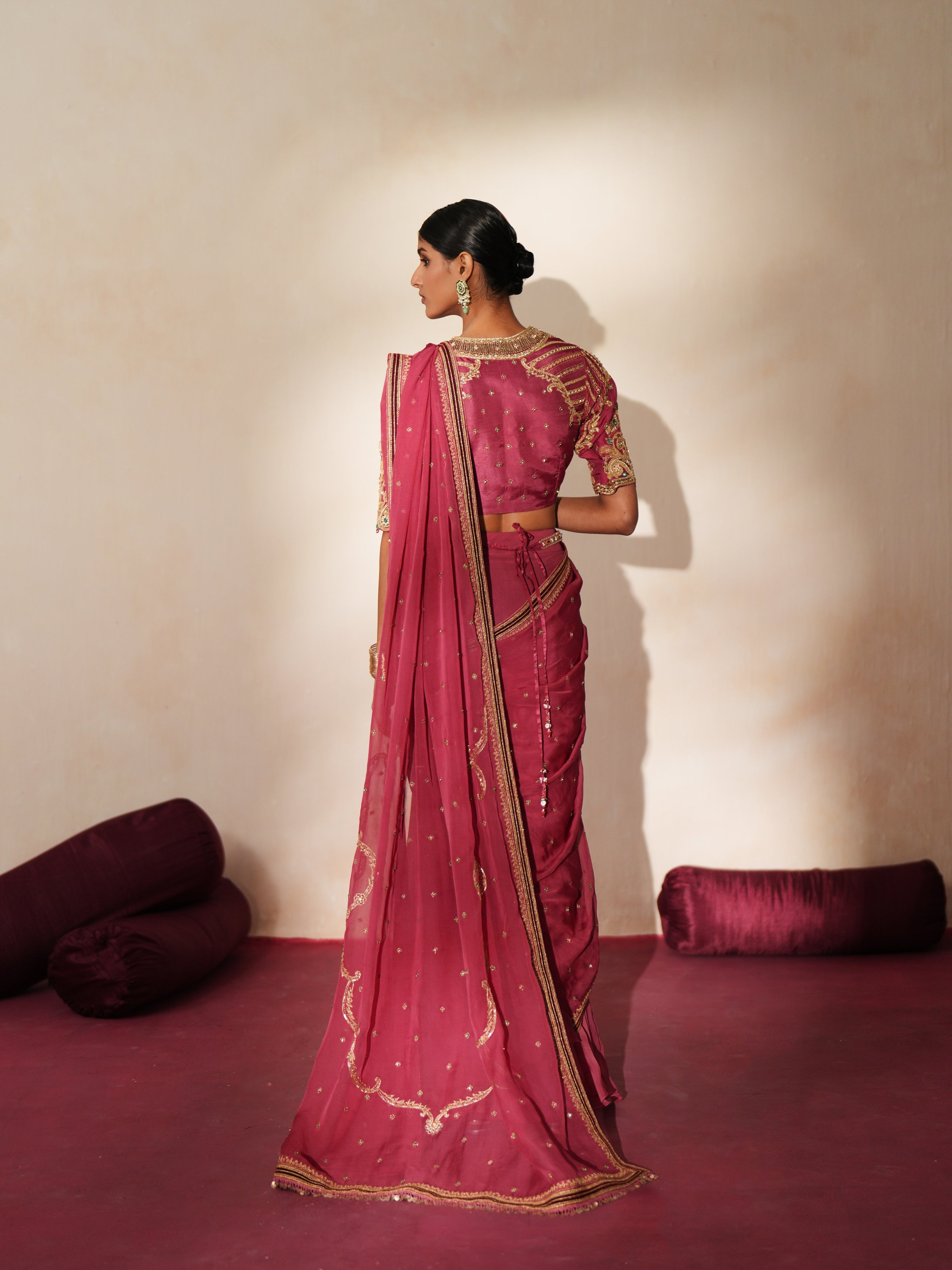 Woman in a mauve pink traditional outfit standing againsta beige wall on a red carpet.