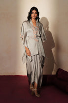 Woman in a mettalic grey traditional outfit standing againsta beige wall on a red carpet.