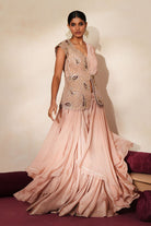 Woman in a soft pink traditional outfit standing againsta beige wall on a red carpet.