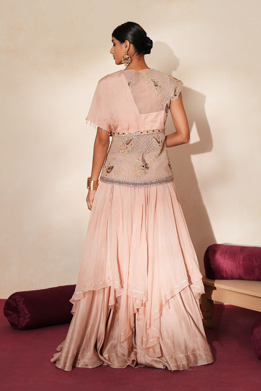 Woman in a soft pink traditional outfit standing againsta beige wall on a red carpet.