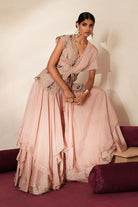 Woman in a soft pink traditional outfit standing againsta beige wall on a red carpet.
