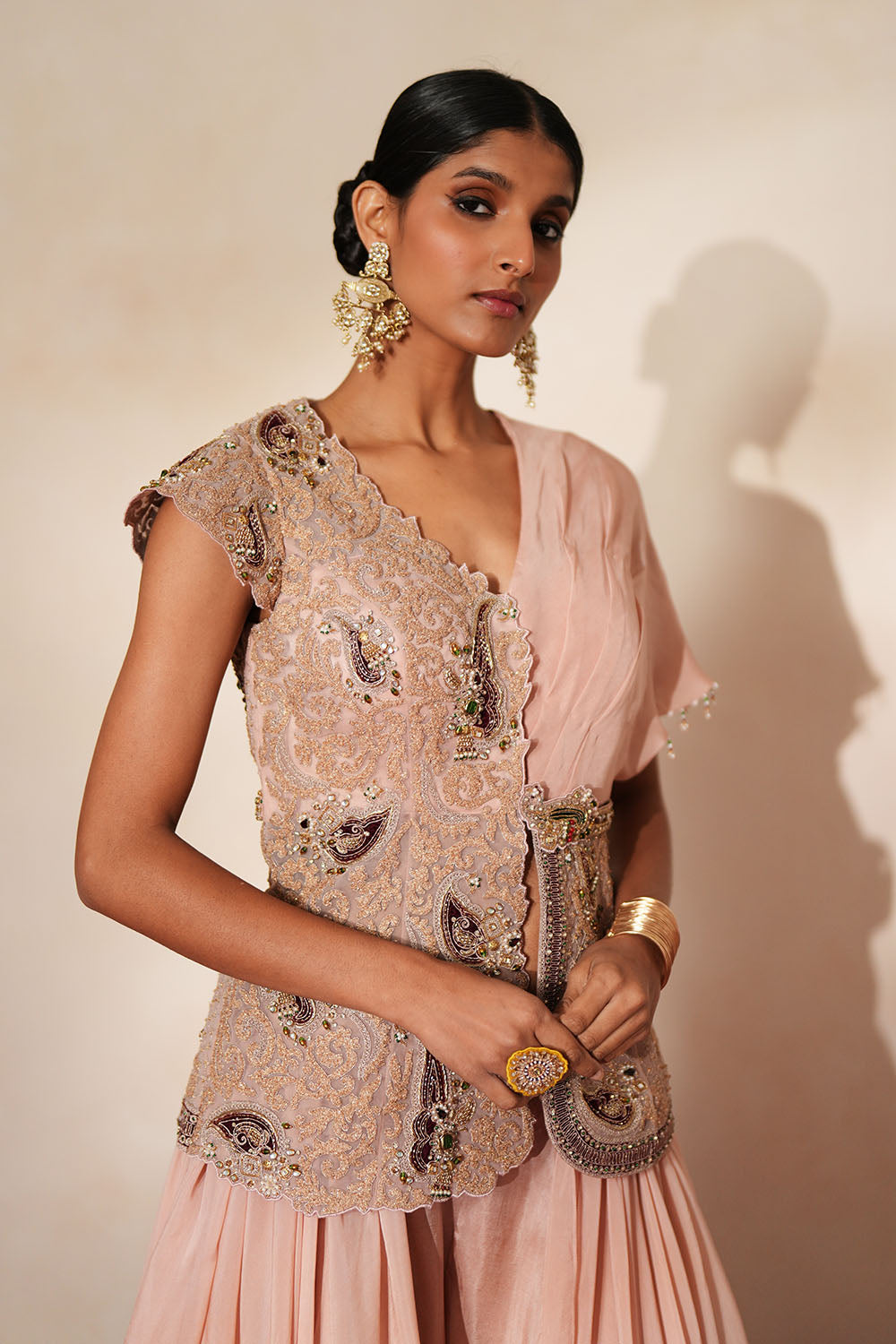 Woman in a soft pink traditional outfit standing againsta beige wall on a red carpet.