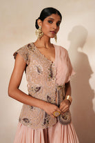 Woman in a soft pink traditional outfit standing againsta beige wall on a red carpet.