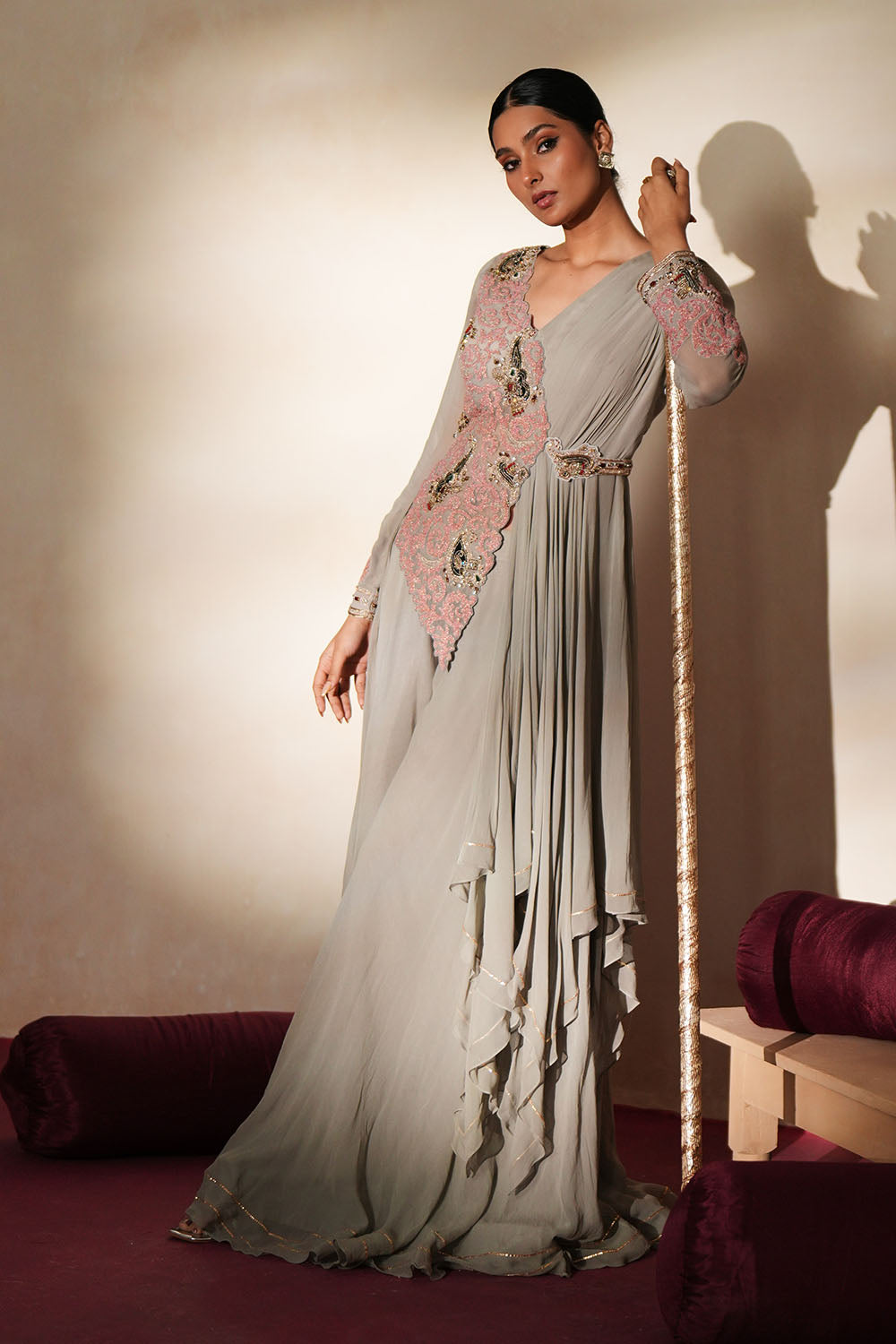 Woman in a mettalic grey traditional outfit standing againsta beige wall on a red carpet.