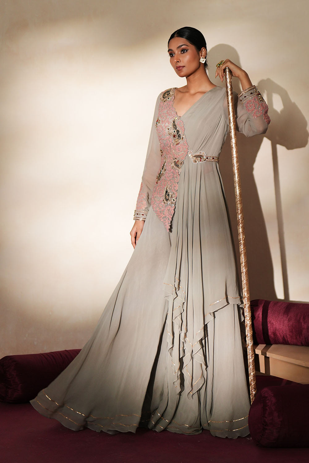 Woman in a mettalic grey traditional outfit standing againsta beige wall on a red carpet.