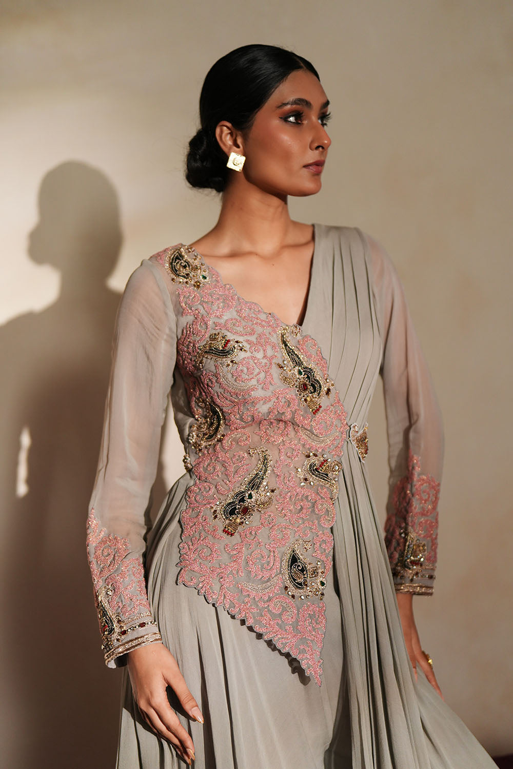 Woman in a mettalic grey traditional outfit standing againsta beige wall on a red carpet.