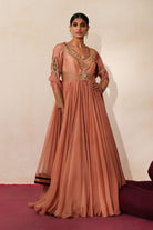 Woman in a metallic mocha  traditional outfit standing againsta beige wall on a red carpet.