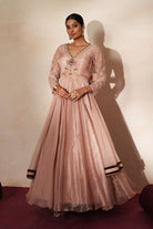 Woman in a soft pink traditional outfit standing againsta beige wall on a red carpet.