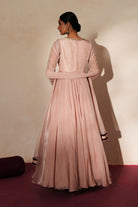 Woman in a soft pink traditional outfit standing againsta beige wall on a red carpet.