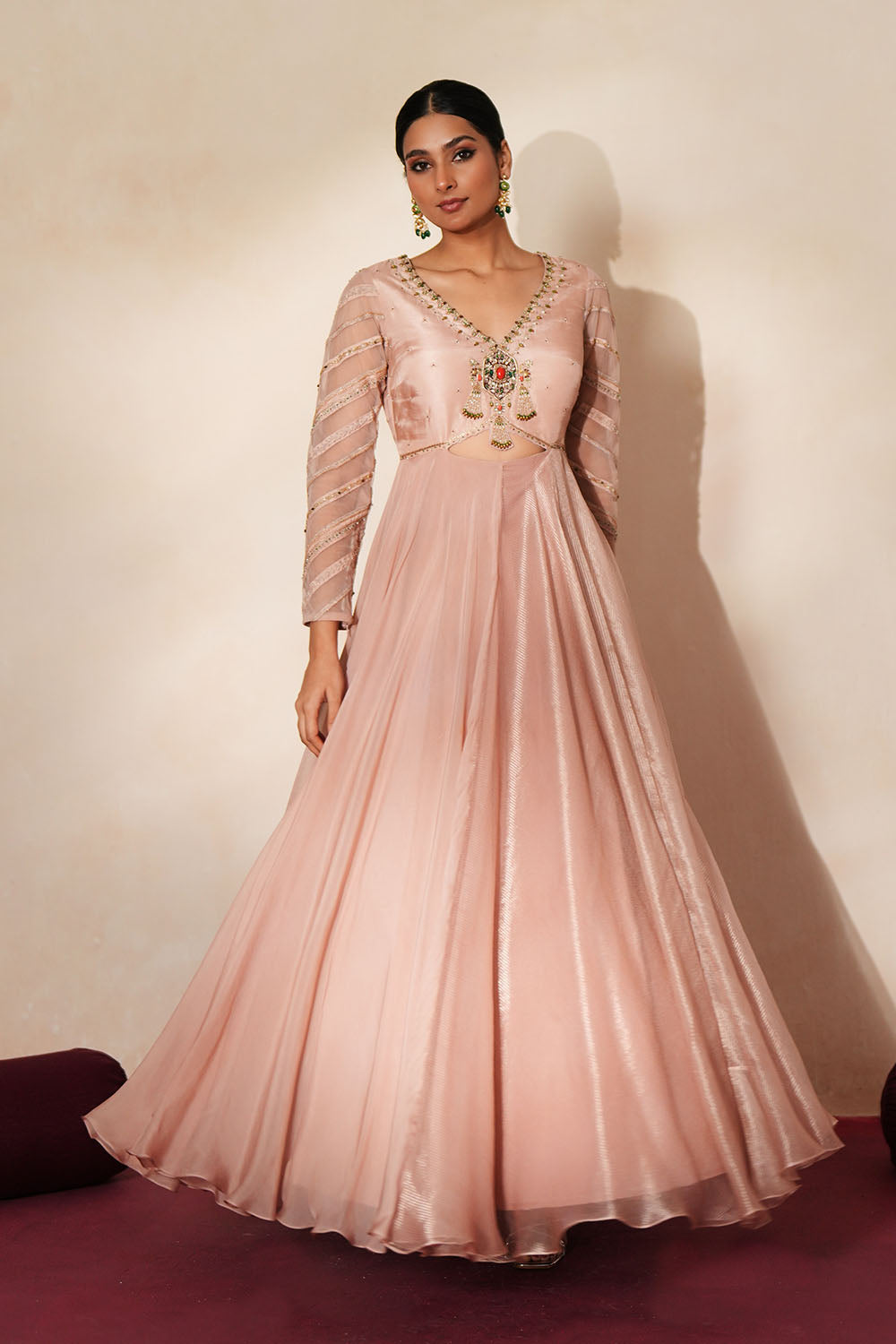 Woman in a soft pink traditional outfit standing againsta beige wall on a red carpet.