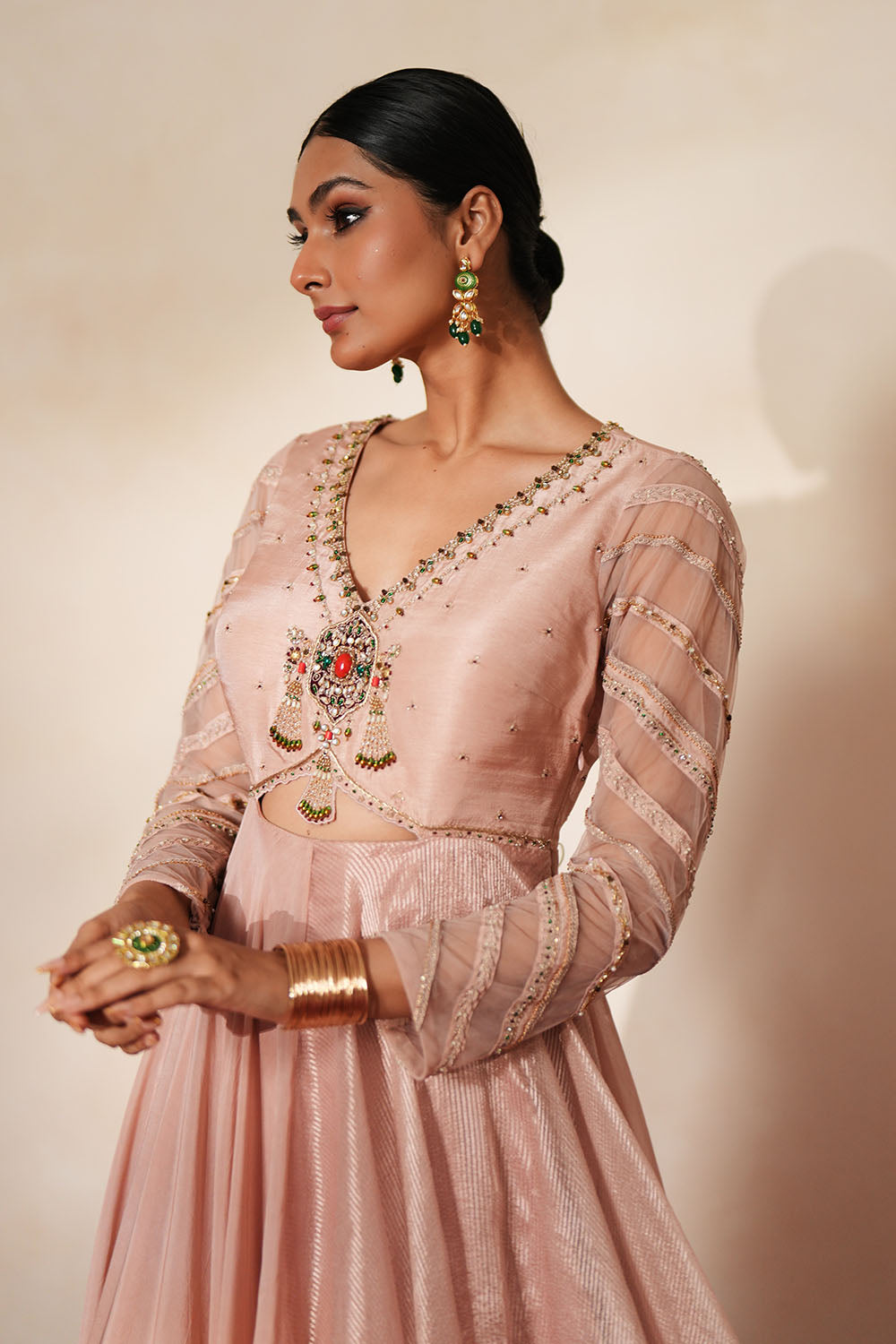 Woman in a soft pink traditional outfit standing againsta beige wall on a red carpet.