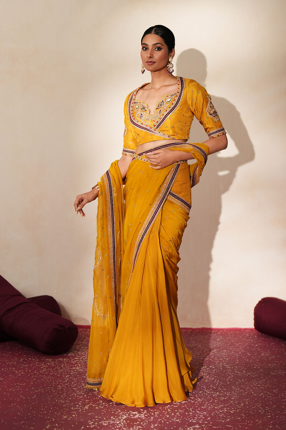 Woman in a golden yellow traditional outfit standing againsta beige wall on a red carpet.