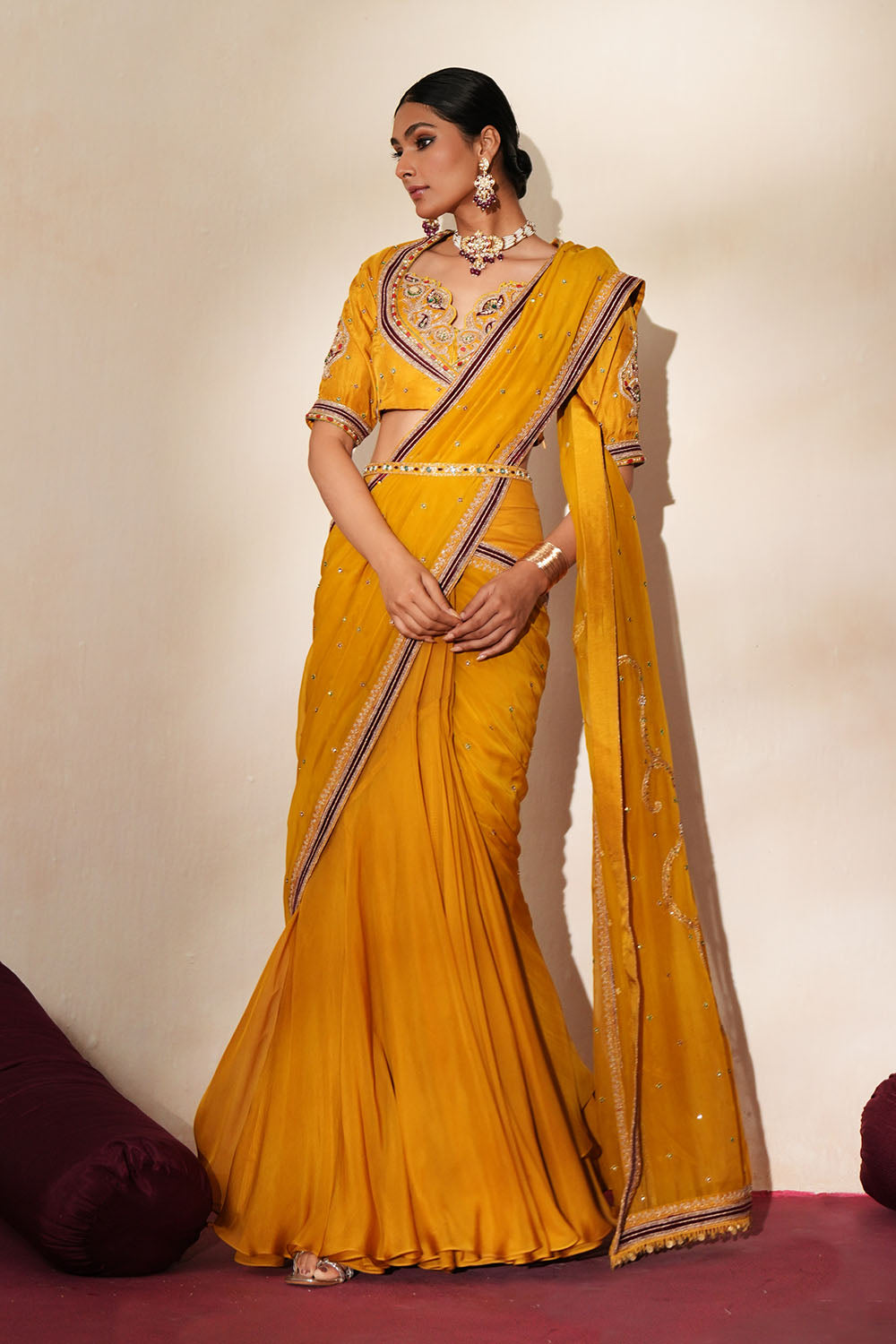 Woman in a golden yellow traditional outfit standing againsta beige wall on a red carpet.