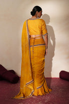 Woman in a golden yellow traditional outfit standing againsta beige wall on a red carpet.