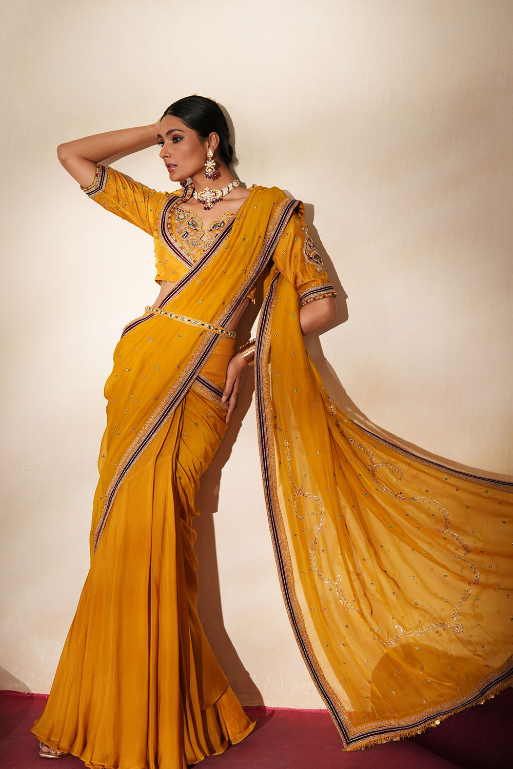 Woman in a golden yellow traditional outfit standing againsta beige wall on a red carpet.