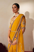 Woman in a golden yellow traditional outfit standing againsta beige wall on a red carpet.