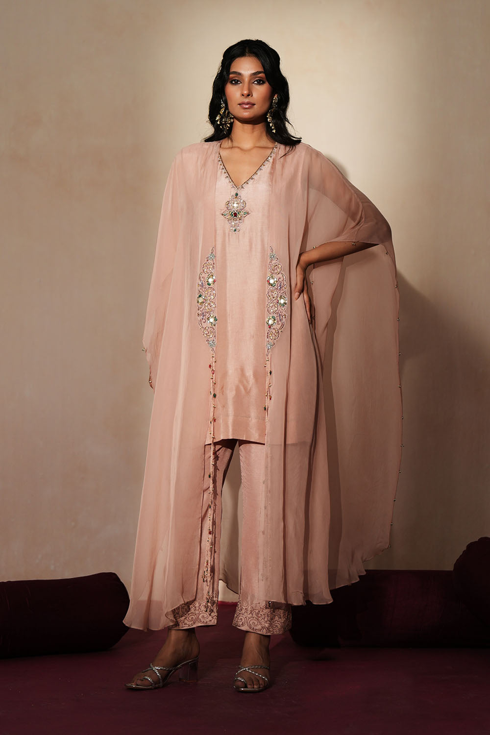 Woman in a soft pink traditional outfit standing againsta beige wall on a red carpet.