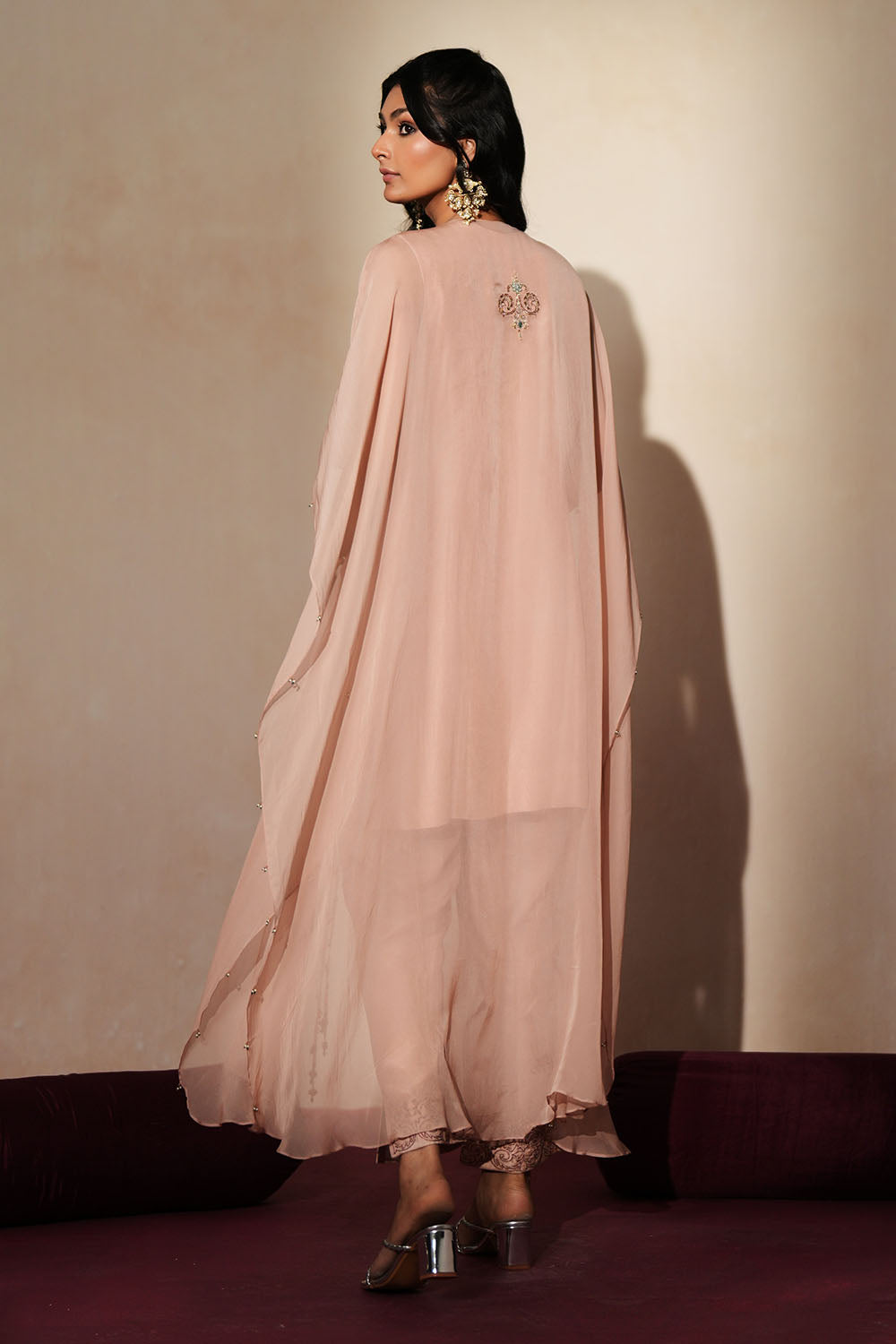 Woman in a soft pink traditional outfit standing againsta beige wall on a red carpet.