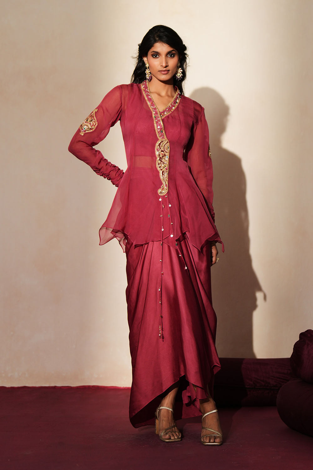 Woman in a mauve pink traditional outfit standing againsta beige wall on a red carpet.